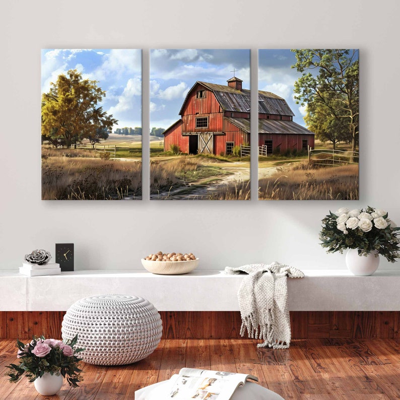 May include: A three-panel canvas art piece depicting a rural landscape with a red barn as the focal point. The barn is surrounded by fields, trees, and a dirt path. The sky is blue with fluffy clouds. The artwork is displayed above a white shelf.
