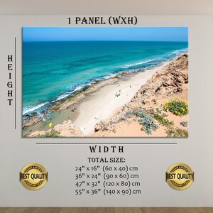May include: A canvas print of a coastal landscape featuring a turquoise ocean, sandy beach, and rocky cliffs under a clear blue sky. The print is displayed on a white wall, with text indicating various size options in inches and centimeters.