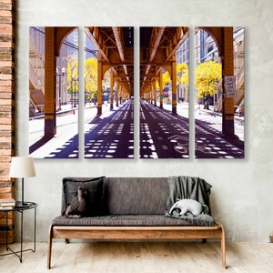 May include: A three-panel photo print of a city street with a yellow metal structure overhead. The street is empty and the sun is shining, casting shadows on the pavement. A sign reads "Bike Lane".