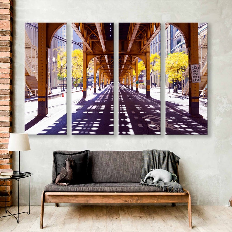 May include: A three-panel photo print of a city street with a yellow metal structure overhead. The street is empty and the sun is shining, casting shadows on the pavement. A sign reads "Bike Lane".