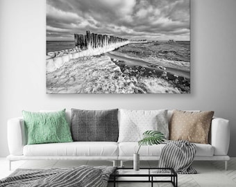 Puede incluir: Una fotografía en blanco y negro de un rompeolas de madera que se extiende hacia el mar. El agua está agitada y el cielo está nublado. El rompeolas está cubierto de hielo y nieve.