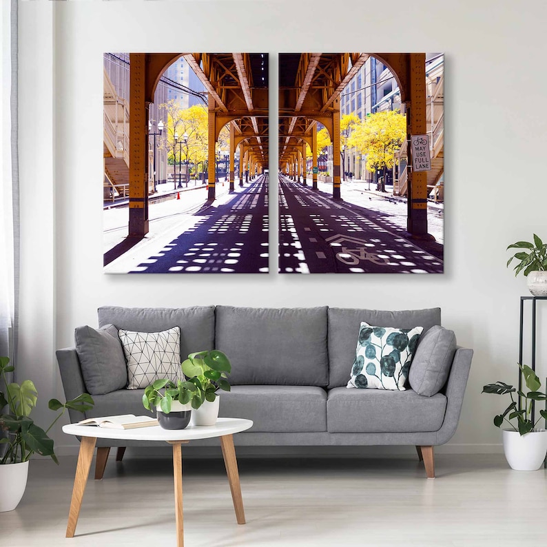 May include: A split-level photograph of a city street under a yellow bridge. The street is lined with trees and the sidewalk is visible. The street is empty and the sun is shining. The sign reads "May Use Full Lane".