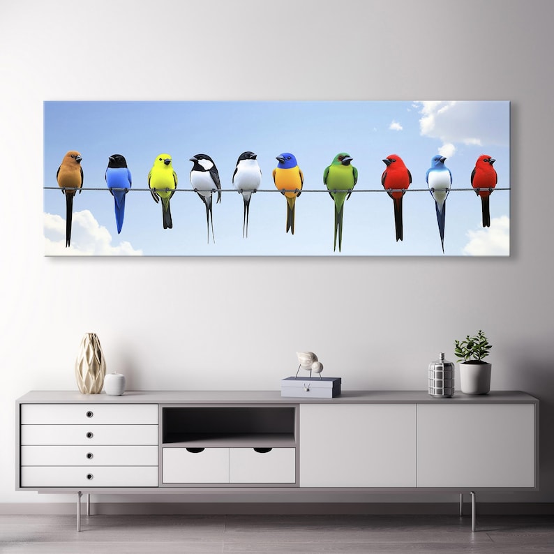 May include: A vibrant panoramic canvas print features ten colorful birds perched on a wire against a light blue sky. The birds are in a row, each a different color: orange, blue, yellow, black and white, white, blue, green, red, blue, and red.  The birds are depicted realistically, showcasing their unique plumage and postures. This horizontal artwork is ideal for adding a pop of color and nature-inspired charm to any space.