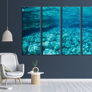 May include: A four-panel canvas art piece depicting an underwater scene. The artwork showcases a turquoise-colored underwater environment with rounded rocks on the seabed. The water's surface is visible above, creating a serene and natural aesthetic.