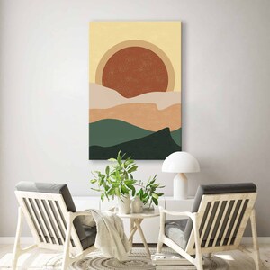 May include: Abstract landscape art print featuring a large rust-colored sun over layered hills in shades of beige, tan, and green. The artwork has a textured, grainy appearance and is displayed on a white wall.