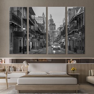 May include: A black and white canvas print set depicting a street scene with buildings and balconies. The image shows a street with cars and buildings with balconies. The artwork is displayed above a bed in a bedroom.