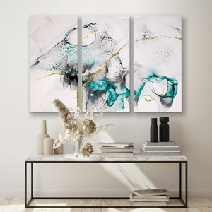 May include: A three-piece abstract art print set featuring a white background with teal and black swirls and gold accents. The prints are displayed on a white marble console table with a black metal frame.