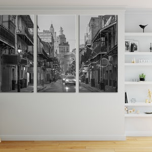 May include: Black and white triptych canvas print of a city street at night. The image features buildings with balconies and streetlights, with a car driving down the wet street. The overall scene is a moody, urban landscape.