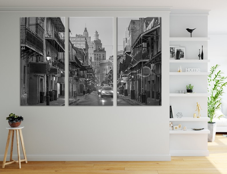 May include: Black and white triptych canvas print of a city street at night. The image features buildings with balconies and streetlights, with a car driving down the wet street. The overall scene is a moody, urban landscape.