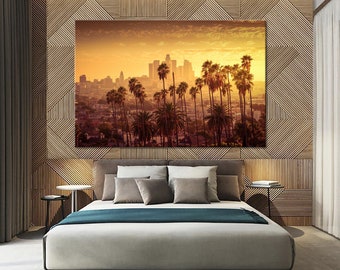 May include: A panoramic view of the Los Angeles skyline at sunset, with palm trees in the foreground and the city's skyscrapers in the background. The sky is a vibrant orange and yellow, and the sun is setting behind the city.