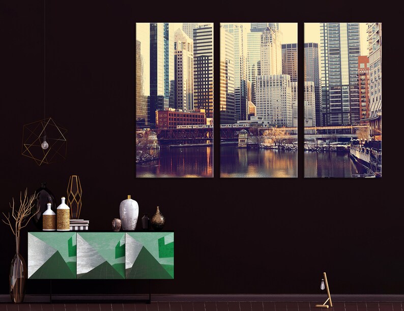 May include: A three-panel canvas print featuring a cityscape with tall buildings, a river, and a bridge. The buildings are a mix of modern and traditional styles, and the river is reflecting the light of the setting sun. The print is in a vintage style, with a warm color palette.
