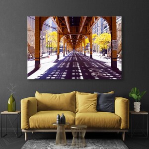 May include: A photograph of a city street under a bridge. The street is lined with trees and the bridge is made of metal. The sun is shining and the shadows of the bridge are cast on the street. The sign on the right side of the image reads "May Use Full Lane".