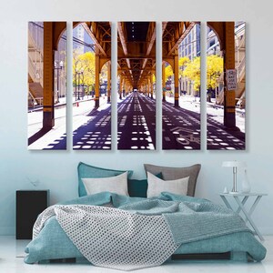 May include: A five-panel canvas print of a city street scene. The street is under a yellow metal overpass with a bike lane. The street is lined with trees and buildings. The sun is shining and the shadows of the overpass are visible on the street.