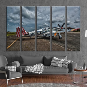 Puede incluir: Un avi&oacute;n militar vintage, un P-51 Mustang, pintado en plata y gris con marcas rojas, blancas y azules, est&aacute; estacionado en una pista. El avi&oacute;n tiene una h&eacute;lice y una gran aleta de cola. El cielo est&aacute; nublado y el suelo est&aacute; pavimentado.