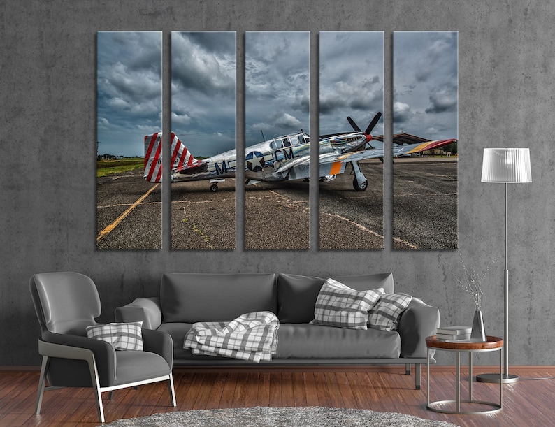 Puede incluir: Un avi&oacute;n militar vintage, un P-51 Mustang, pintado en plata y gris con marcas rojas, blancas y azules, est&aacute; estacionado en una pista. El avi&oacute;n tiene una h&eacute;lice y una gran aleta de cola. El cielo est&aacute; nublado y el suelo est&aacute; pavimentado.