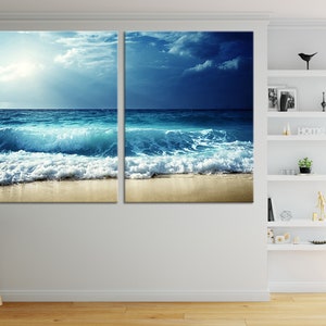 K&ouml;nnte beinhalten: Ein geteilter Leinwanddruck mit einer Meereslandschaft mit blauem Wasser, wei&szlig;en, schaumigen Wellen, die an einem Sandstrand brechen, und einem bew&ouml;lkten Himmel.