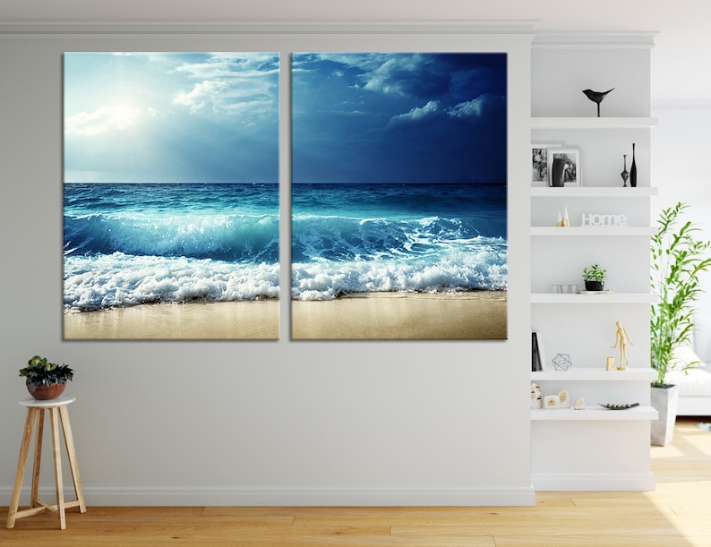 K&ouml;nnte beinhalten: Ein geteilter Leinwanddruck mit einer Meereslandschaft mit blauem Wasser, wei&szlig;en, schaumigen Wellen, die an einem Sandstrand brechen, und einem bew&ouml;lkten Himmel.