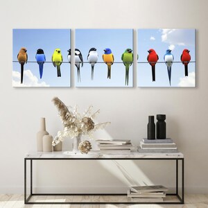 May include: Triptych wall art featuring colorful birds perched on a wire against a light blue sky. The birds are in shades of red, yellow, blue, and green.  The artwork is divided into three panels, each showing a different arrangement of the birds. The birds are depicted in a realistic style, with detailed feathers and vibrant colors. This is a nature-themed artwork suitable for home decor.