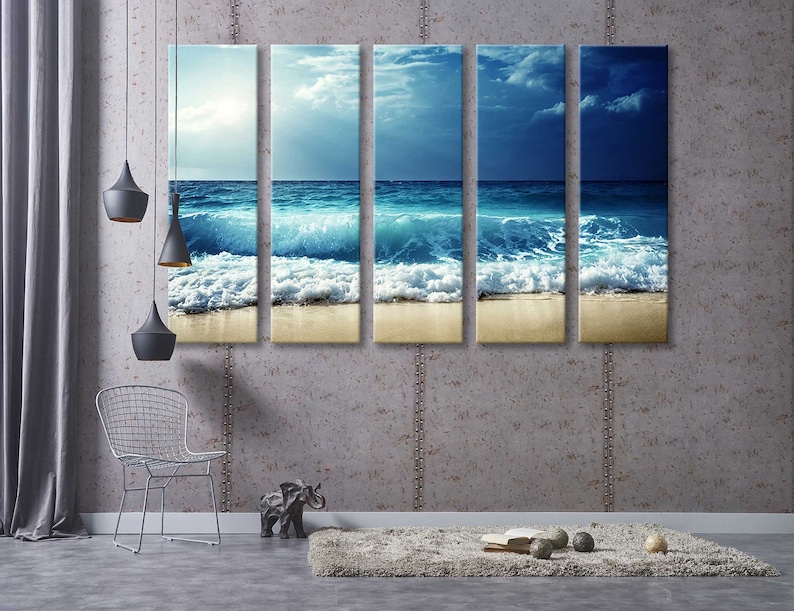 K&ouml;nnte beinhalten: Ein f&uuml;nfteiliger Leinwanddruck, der eine Meereslandschaft mit blauen Ozeanwellen zeigt, die an einem Sandstrand brechen. Der Himmel ist hellblau mit wei&szlig;en Wolken.