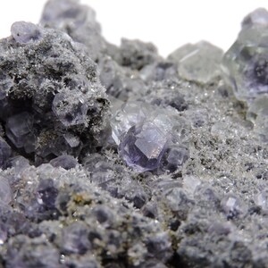 May include: A mineral specimen featuring clusters of translucent, purple, cubic fluorite crystals embedded within a rough, grey, granular matrix. The crystalline structures exhibit geometric facets and varying levels of clarity across the surface.