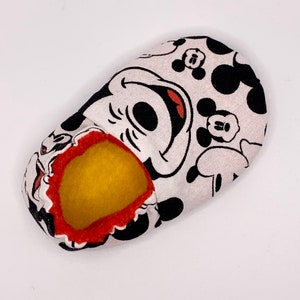 May include: A white fabric slipper with a black and red Mickey Mouse design. The slipper has a yellow felt lining.