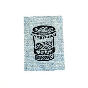 May include: A black and white illustration of a jam jar with the word "JAM" on a denim patch. The jar has a decorative lid and a label around the middle. The denim patch is light blue.