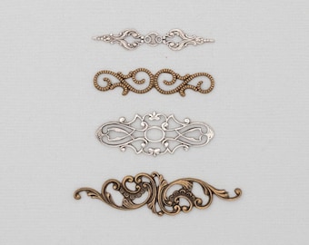 May include: Four ornate metal embellishments in silver, bronze, and gold tones are arranged on a light gray background. The decorative pieces feature intricate scrollwork and symmetrical designs, suitable for craft projects.