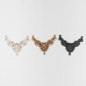 May include: Three decorative metal corner brackets in silver, antique brass, and black. Each bracket features an ornate, symmetrical design with scrollwork and small holes for attachment. Ideal for furniture or craft projects.