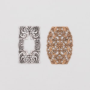 May include: Two ornate metal embellishments. One is rectangular with a silver finish and a central cutout. The other is oval-shaped with a gold finish and a floral design. Both feature intricate scrollwork and decorative details.
