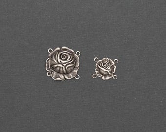 May include: Two silver-toned rose charms, one large and one small, are displayed against a dark gray background. Each charm features a detailed rose design with visible petals and connecting loops for jewelry making or crafting projects.