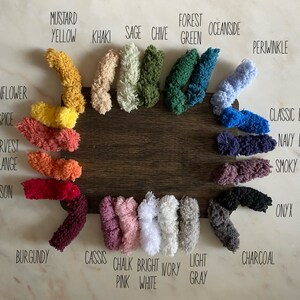 Op de afbeelding: Een kleurenkaart met garenstalen met namen zoals "Mosterdgeel", "Salie", "Bosgroen", "Zeezijde", "Blauwe druif", "Klassiek blauw", "Donkerblauw", "Rokerige amethist", "Onyx", "Antraciet", "Cassis", "Krijt roze", "Helder wit", "Lichtgrijs", "Bordeaux", "Krimzon", "Oogst oranje", "Pompoenspecerij", en "Zonnebloem".