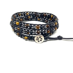 May include: A black leather wrap bracelet with tiger's eye and hematite beads. The bracelet has a silver charm with a paw print.
