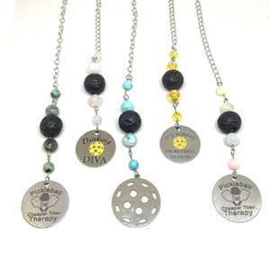 May include: Four different pickleball themed car charms with black lava beads and various colored beads. The charms feature different pickleball sayings, including "Pickleball is Cheaper Than Therapy", "Dinking Diva", and "It's Always Pickleball Season".