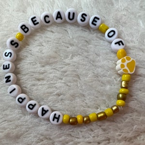 Puede incluir: Un brazalete de cuentas blancas y amarillas con las palabras "Happiness because of" y un dije de huella de pata.