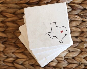 May include: Set of four white marble coasters with a black outline of the state of Texas and a red heart in the center.
