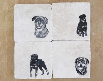 May include: Four square stone coasters with black Rottweiler dog illustrations. Each coaster features a different pose: a headshot, a sitting dog, a standing dog, and a smiling face. The coasters are set against a light brown wooden surface.