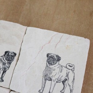 May include: Set of four white marble coasters with black and white illustrations of pugs. Each coaster features a different pug pose.