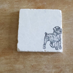 May include: A square, off-white marble coaster with a detailed black and white illustration of a dog. The dog is standing, facing right. The coaster is set against a wooden background.