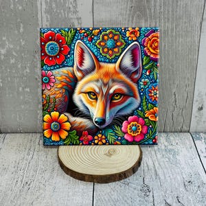 May include: Square canvas art featuring a vibrant fox portrait surrounded by colorful flowers. The fox has orange and white fur with yellow eyes. The flowers are red, orange, pink, and blue, set against a dark blue background.