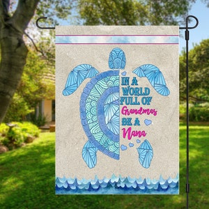 May include: A blue and white patterned sea turtle with the text "In a world full of Grandmas be a Nana" on a beige garden flag with a blue wave border.