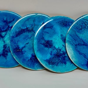 May include: Set of four blue and white resin coasters with a marbled design. The coasters are round and have a glossy finish.
