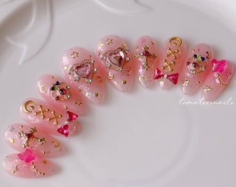 May include: Pink and gold nail art with a variety of charms, including hearts, stars, crosses, and bows. The nail art is on a white background.