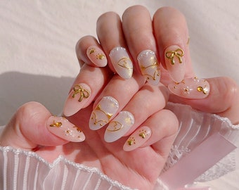 May include: Close-up of a hand with several pink and white almond-shaped nails decorated with gold bows, foxes, and glitter.