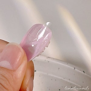 May include: A close-up of a pink nail tip with a clear gel polish applied to the tip.