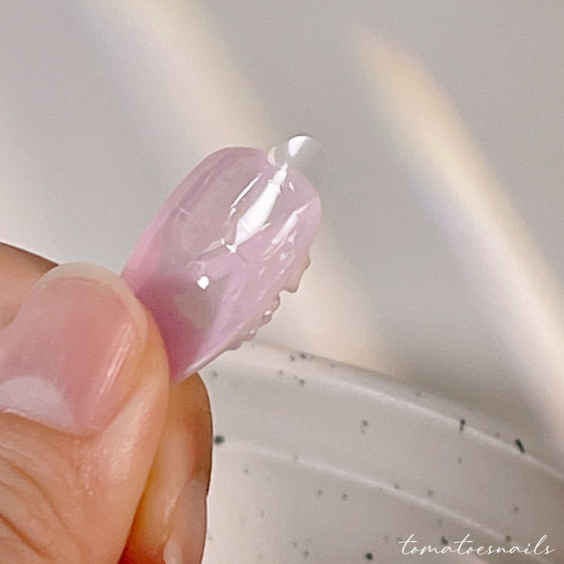 May include: A close-up of a pink nail tip with a clear gel polish applied to the tip.