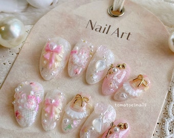 May include: A set of ten pink and white nail art designs featuring bows, pearls, and lace. The designs are on a white background with the text "Nail Art" and "tomatoesnails".