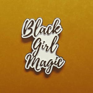 May include: White enamel pin with black lettering that reads "Black Girl Magic".