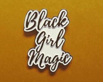 May include: White enamel pin with black lettering that reads "Black Girl Magic".