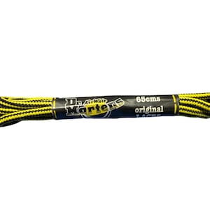 May include: A pair of yellow and black Dr. Martens original laces, 65cms long, coiled on a white background. The laces are in a black and yellow pattern. The product packaging is black with the Dr. Martens logo and product information.