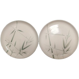 May include: Two round, off-white ceramic plates featuring a painted green bamboo stalk design. Each plate has a smooth, glossy finish with a simple, minimalist aesthetic. The bamboo pattern is rendered in varying shades of green, showing leaves and stems across the surface of the plates.